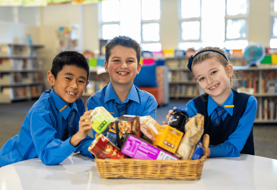 Three students smile at the camera as they show off a lovely Christmas hamper they have made